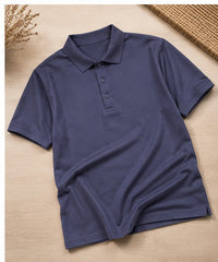 A navy blue short-sleeve polo shirt laid flat on a light wood surface, with dried floral decor and a woven mat partially visible in the corners.
