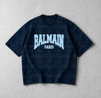 A Balmain Paris short-sleeve t-shirt in dark navy blue with a subtle grid pattern, featuring a light blue and white 'BALMAIN PARIS' logo printed on the chest, laid flat on a light gray background.