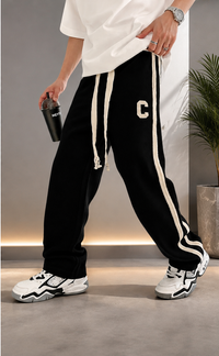 A person wearing black sweatpants with white side stripes and a white drawstring, styled with a white t-shirt and white sneakers in an indoor setting.