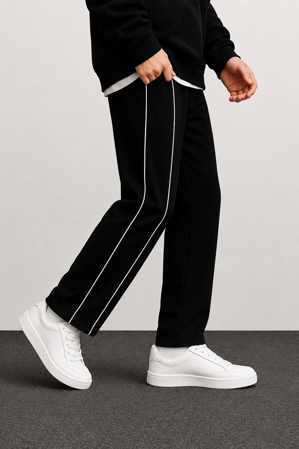 Black track pants with white side stripes, worn by a model with white sneakers against a neutral studio background.