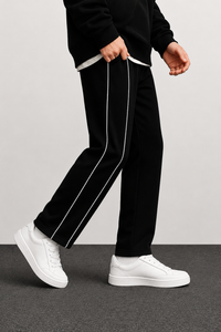 Black track pants with white side stripes, worn by a model with white sneakers against a neutral studio background.