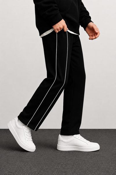 Black track pants with white side stripes, worn by a model with white sneakers against a neutral studio background.