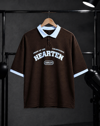 A dark brown short-sleeve polo shirt with a light blue collar and sleeve cuffs, featuring a white graphic print on the front that reads 'PRIDE OF THE COLOEBSTRAIC HEARTEN' and 'ARMANI'. The shirt is displayed on a wooden hanger against a dark gray background with studio lighting equipment visible on the sides.