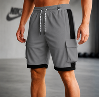 Gray athletic cargo shorts with black side panels, black hem, and a white-and-black drawstring, shown on a cropped male model in a gym setting.