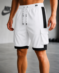 White athletic cargo shorts with black side panels, black hem trim, and a black-and-white drawstring, shown on a model in a gym setting.