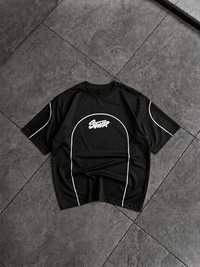 A black short-sleeve t-shirt with white piping and a white 'Scout' logo on the chest, laid flat on a dark gray tiled floor.
