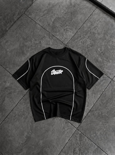A black short-sleeve t-shirt with white piping and a white 'Scout' logo on the chest, laid flat on a dark gray tiled floor.