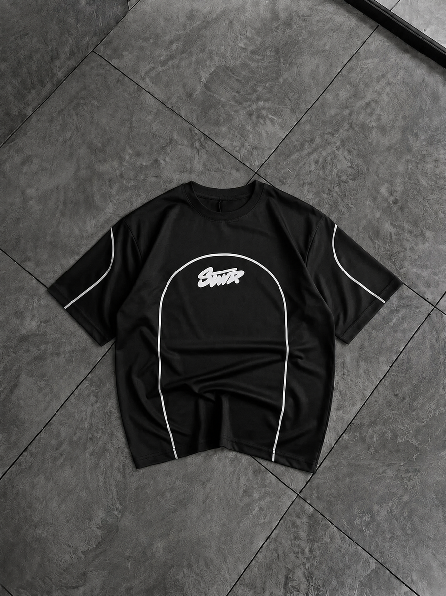 A black short-sleeve t-shirt with white piping and a white 'Scout' logo on the chest, laid flat on a dark gray tiled floor.
