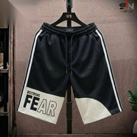 Black athletic shorts with white side stripes, a white lower panel, and 'BESTROONG FEAR' printed on one leg, hanging on a black hanger against a brown textured backdrop.