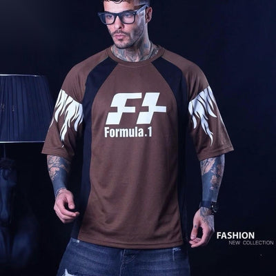 A man wearing a brown short-sleeve t-shirt with black side panels, white flame graphics on the sleeves, and a large white 'F1 Formula.1' logo on the chest, set against a dark background.