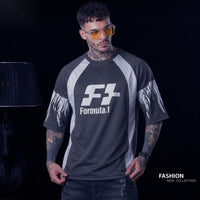 A man wearing a dark gray and white Formula.1 short-sleeve t-shirt with flame patterns on the sleeves, posed against a dark studio background with a lamp on the left.