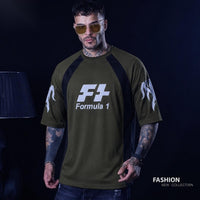 A man wearing an olive green short-sleeve t-shirt with black raglan sleeves and white 'Formula 1' graphics on the chest and sleeves, posed against a dark studio background.