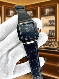 Black wristwatch held by a gloved hand with a store display in the background