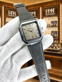Gray wristwatch held by a gloved hand with a jewelry store background