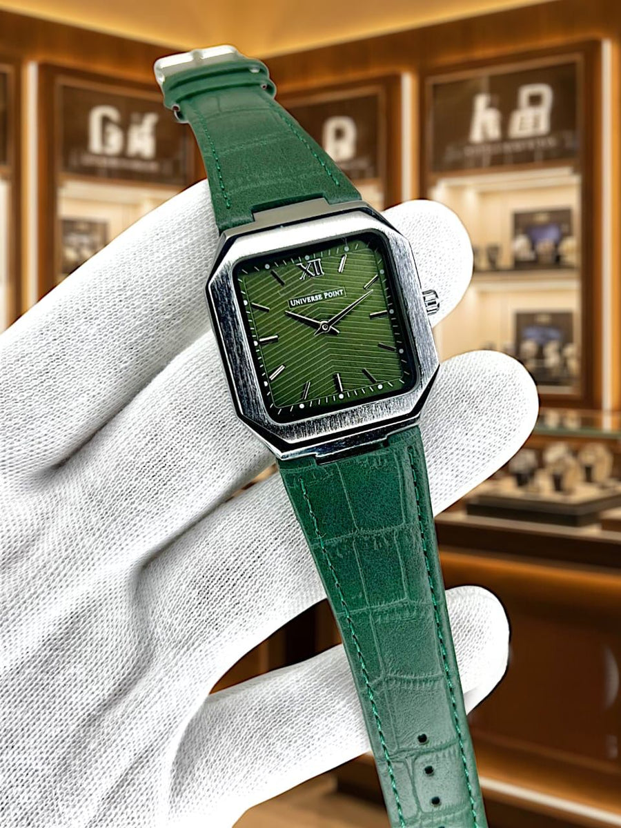 Green wristwatch with a detailed face held by a gloved hand against a blurred background.