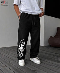 A person wearing black drawstring sweatpants with a white graphic print on the lower left leg, paired with a white t-shirt and white sneakers, standing on a gray wooden deck.