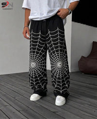 Black wide-leg sweatpants with a white spiderweb pattern on the legs, worn by a model standing on a gray wooden deck.