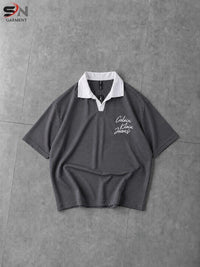 A dark gray short-sleeve polo shirt with a white collar and white script embroidery on the left chest, laid flat on a gray tiled surface.