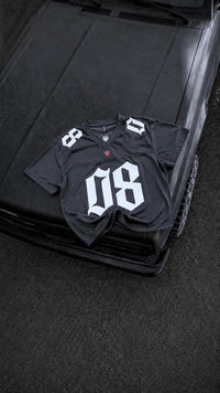 A black football-style jersey with large white '08' lettering on the front and white shoulder numbers, laid flat on the hood of a black vehicle.