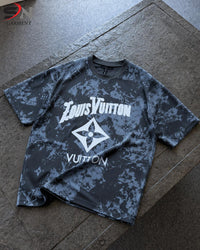 A short-sleeve t-shirt with a dark gray and black camouflage pattern and a large white logo graphic on the front, laid flat on a stone surface.