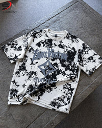  short-sleeve t-shirt with a black and white abstract graphic print and a large gray logo on the front, laid flat on a gray stone surface.