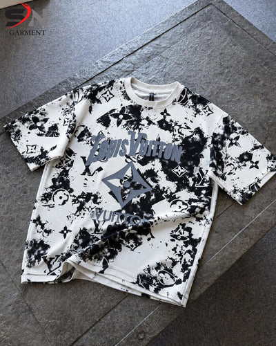  short-sleeve t-shirt with a black and white abstract graphic print and a large gray logo on the front, laid flat on a gray stone surface.
