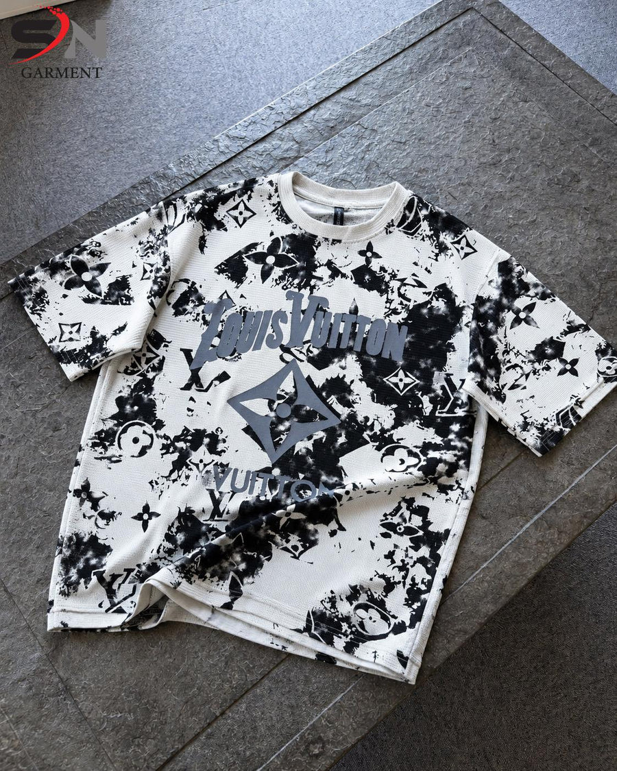  short-sleeve t-shirt with a black and white abstract graphic print and a large gray logo on the front, laid flat on a gray stone surface.