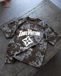 A brown and gray camouflage t-shirt with a white Louis Vuitton graphic on the front, laid flat on a dark gray stone surface.
