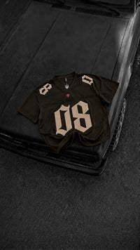 A dark olive green football-style jersey with beige numbers 8 and 08, laid flat on the hood of a black vehicle.