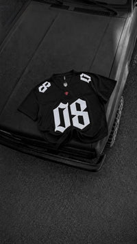 Black oversized men's graphic jersey t-shirt with bold white 08 print, premium streetwear fashion displayed on a black vintage car hood.