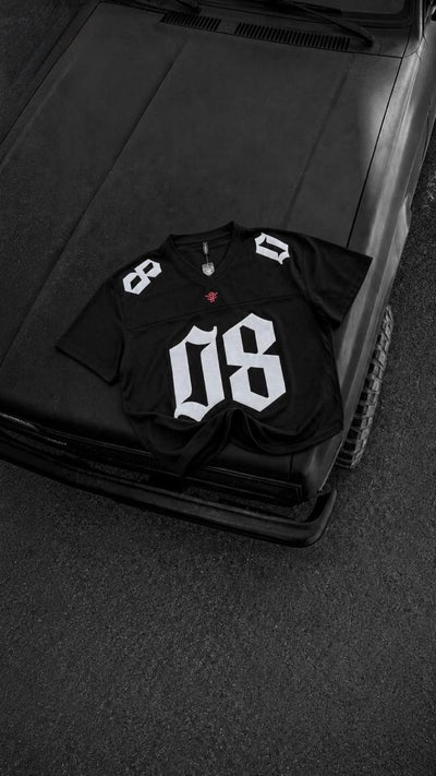 Black oversized men's graphic jersey t-shirt with bold white 08 print, premium streetwear fashion displayed on a black vintage car hood.