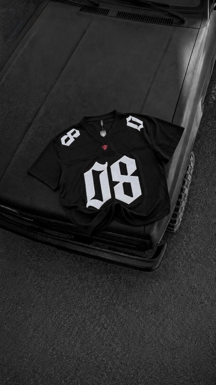 Black oversized men's graphic jersey t-shirt with bold white 08 print, premium streetwear fashion displayed on a black vintage car hood.