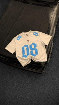 Cream oversized men's graphic jersey t-shirt with bold sky blue 08 print, premium streetwear fashion displayed on a black vintage car hood.