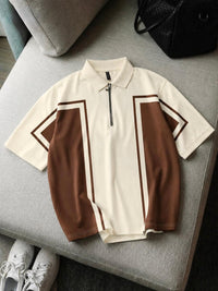 A short-sleeve polo shirt with a half-zip collar, featuring a cream base with brown color-blocked panels and thin brown stripe accents, laid flat on a gray upholstered ottoman.