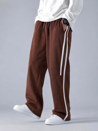 A person wearing brown wide-leg sweatpants with white side stripes, styled with a white long-sleeve top and white sneakers against a light gray studio background.