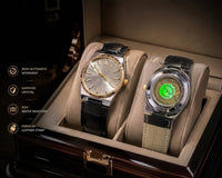Two luxury wristwatches displayed in a dark wood presentation box with beige velvet cushions. The left watch has a silver-toned case, a champagne dial, and a black leather strap.