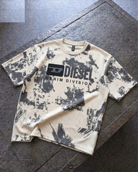 A Diesel Denim Division short-sleeve t-shirt with a black and off-white paint splatter pattern, laid flat on a dark gray stone surface.