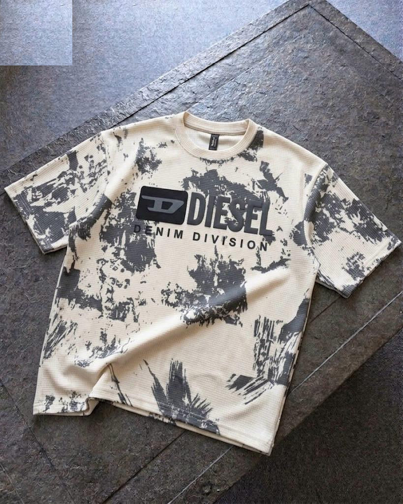 A Diesel Denim Division short-sleeve t-shirt with a black and off-white paint splatter pattern, laid flat on a dark gray stone surface.