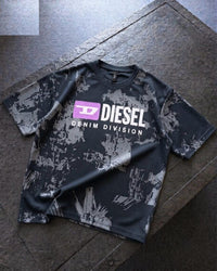 A Diesel Denim Division short-sleeve t-shirt with a black and gray distressed paint splatter pattern, featuring a purple and white logo on the chest, laid flat on a dark stone surface.