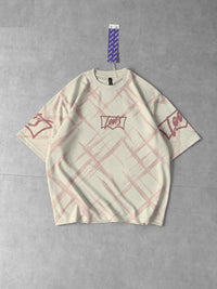 A cream-colored Levi's short-sleeve t-shirt with a pink plaid pattern and red graphic prints on the chest and sleeves, laid flat on a gray concrete floor.