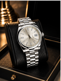 A silver stainless steel wristwatch with a cream-colored dial and date window, resting on a black leather display cushion inside a black presentation box with gold trim.
